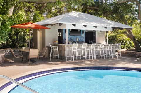 Poolside bar cabana with white umbrella, seating area, and swimming pool in foreground