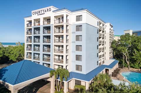 White multi-story Courtyard hotel building with balconies, pool, and ocean view in background