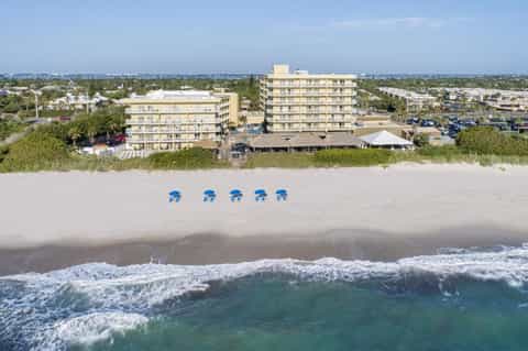 Oceanfront hotel buildings with blue umbrellas on sandy beach and crashing waves in foreground