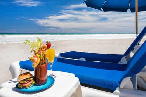 Beach lounge setup with blue chairs, umbrella, cocktails, and burger