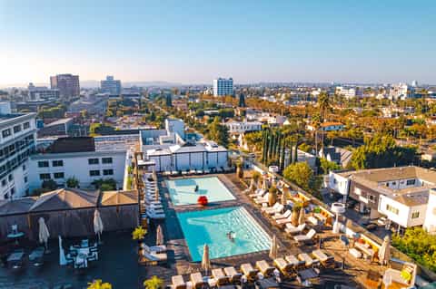 Aerial view of rooftop pool and lounging area overlooking a sprawling city landscape with mountains