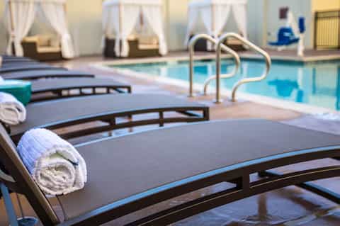 Indoor pool area with lounge chairs, rolled towels, pool railings, and cabana-style drapes