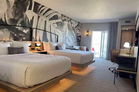 Modern hotel bedroom with two queen beds, striped bedding, botanical wall mural, and balcony access