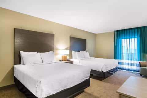 Hotel room with two queen beds, beige walls, turquoise curtains, and modern furnishings