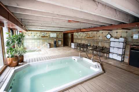 Indoor hot tub spa area with wooden deck, exposed beams, seating, and tile walls