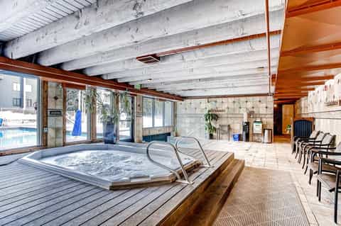 Indoor spa facility with hot tub, lounge chairs, and large windows overlooking outdoor pool area