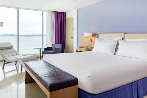 Modern beachfront hotel room with king bed, ocean view balcony, and contemporary furnishings