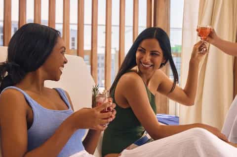 Two women toasting with cocktails in a hotel room with city views