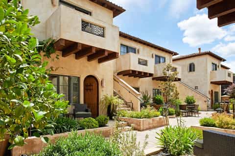 Tuscan-style resort courtyard with terracotta buildings, wooden doors, landscaped gardens, and outdoor seating