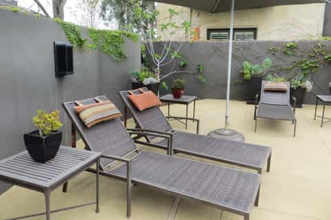Outdoor courtyard with lounge chairs, umbrella, potted plants, and ivy-covered gray walls
