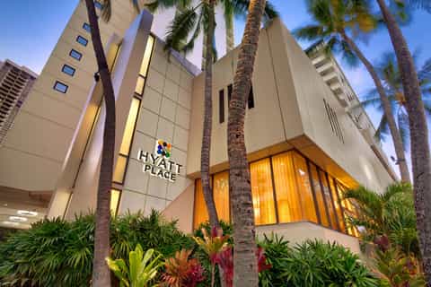 Hyatt Place hotel exterior at dusk with illuminated entrance, palm trees, and tropical landscaping
