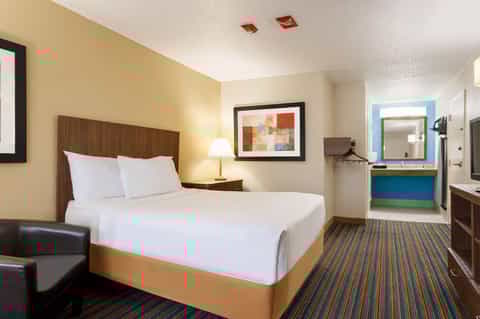 Hotel bedroom with yellow accent wall, brown wooden headboard, white bedding, and blue bathroom entrance