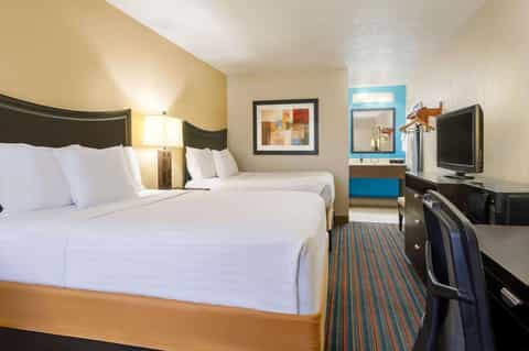 Hotel guest room with two queen beds, black headboards, desk with blue accent, striped carpet