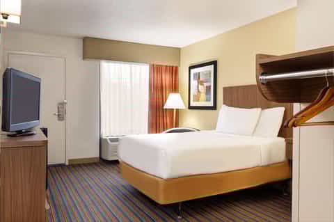 Hotel room with queen bed, wood headboard, flat-screen TV, and window with orange curtains