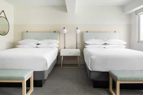 Modern hotel room with two queen beds, natural wood headboards, and minimalist decor