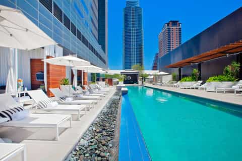 Modern rooftop pool with turquoise water, white loungers, and tall buildings in urban downtown setting