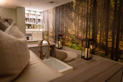 Luxury spa bathroom with soaking tub, forest mural wallpaper, and white shelving unit
