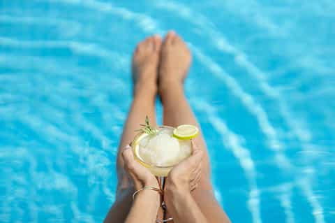 Person relaxing poolside holding a refreshing cocktail with lime garnish