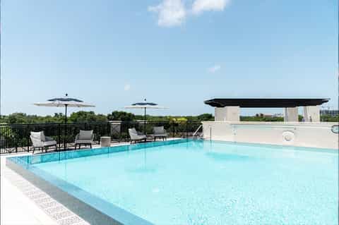 Rooftop pool with lounge chairs, umbrellas, and city skyline view on clear day