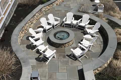 Overhead view of circular fire pit seating area with white Adirondack chairs on stone patio