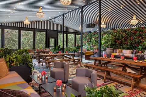 Elegant rooftop lounge with black striped pergola, wooden furniture, flowering plants, and crystal chandeliers