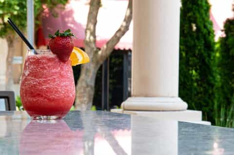 Refreshing strawberry cocktail with orange slice and black straw on outdoor patio table