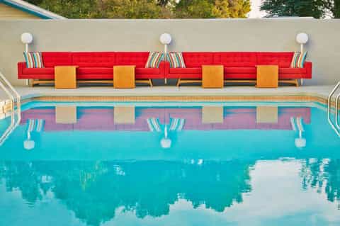 Aerial view of resort pool with bright red lounge seating and turquoise water reflection
