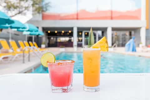 Colorful cocktails at poolside bar with lounge chairs and resort in background