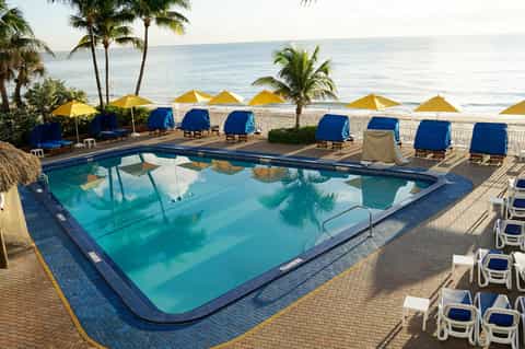 Beachfront swimming pool with blue lounge chairs, yellow umbrellas, and ocean view