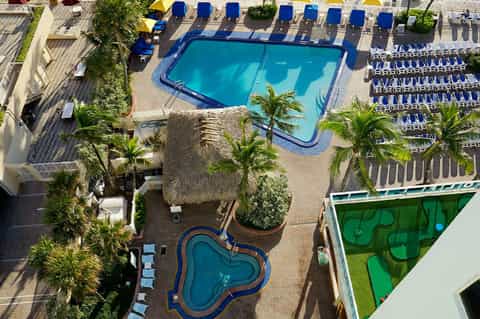 Aerial view of hotel pool surrounded by palm trees, lounge chairs, and resort amenities