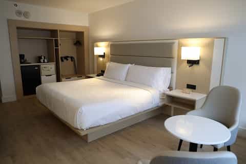 Modern hotel bedroom with king bed, light wood furnishings, and contemporary décor