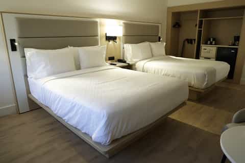 Modern hotel room with two queen beds, neutral bedding, and contemporary furnishings