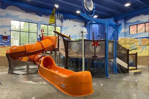 Indoor water park with orange tube slides, splash pools, and nautical-themed wall murals