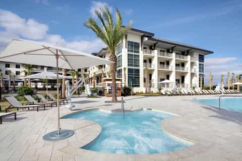 Beachfront resort with pool, spa area, palm trees, and multi-story white building