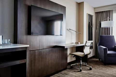 Modern hotel suite with dark wood desk, wall-mounted TV, office chair, and contemporary furnishings