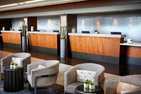 Modern hotel lobby with wooden reception desks, woven accent chairs, and contemporary lighting