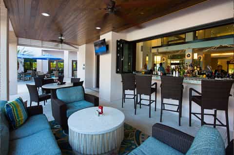 Modern hotel bar and lounge with blue seating, white marble table, dark wood ceiling, and open concept design