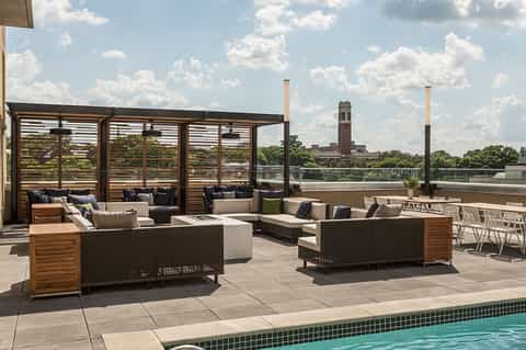 Rooftop terrace with woven lounge seating, wooden pergolas, and city skyline view in background