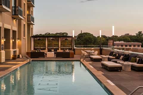Rooftop pool deck at dusk with lounge chairs, ambient lighting, and city skyline views
