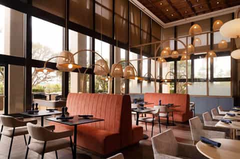 Modern restaurant interior with copper pendant lights, coral banquettes, and floor-to-ceiling windows