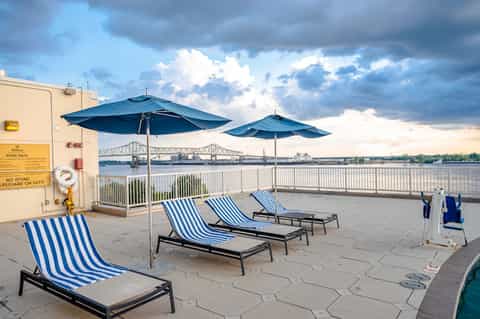 Waterfront deck with blue striped lounge chairs and umbrellas overlooking a bridge and river