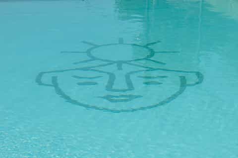 Swimming pool with artistic sun face design visible underwater on pool floor