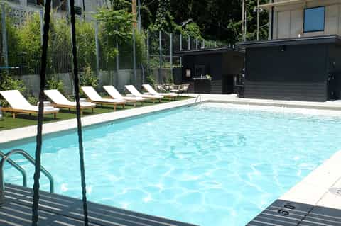 Resort pool with turquoise water, white lounge chairs on grass, black modern pavilion, and green climbing vines