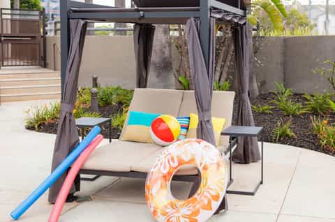 Outdoor cabana lounge with gray curtains, comfortable seating, colorful beach toys and inflatable ring