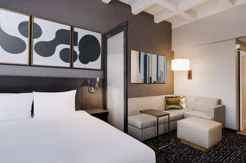 Modern hotel suite with canopy bed, grey sofa, abstract artwork, and contemporary furnishings