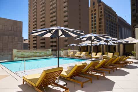 Outdoor pool deck with lounge chairs, navy and white umbrellas, and city skyline backdrop