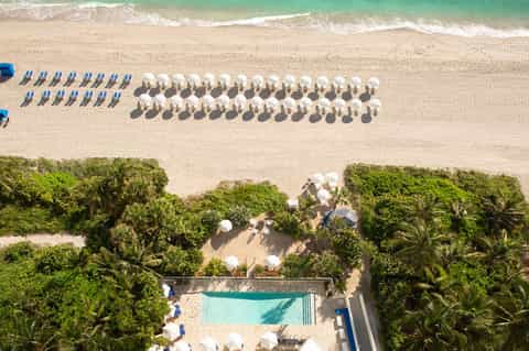 Aerial view of pristine beach with organized rows of white umbrellas, turquoise water, and tropical vegetation