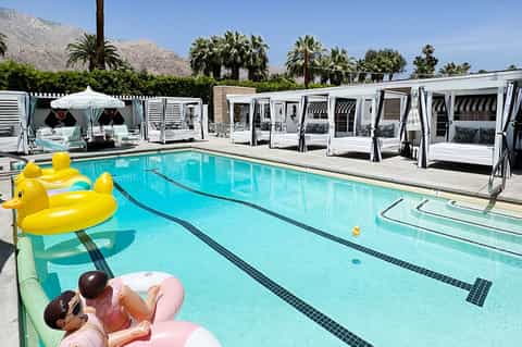 Resort pool with white cabanas, palm trees, and lounge chairs against desert mountain backdrop