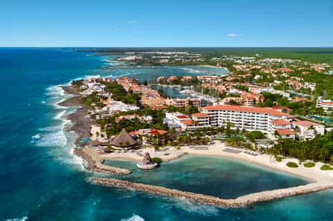 Aerial view of beachfront resort with red-roofed buildings, protected cove, and surrounding tropical vegetation