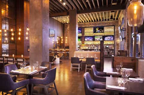 Modern hotel restaurant and bar with industrial design, exposed brick walls, pendant lighting, and contemporary furnishings